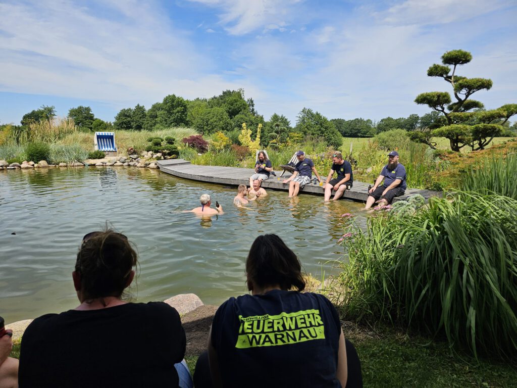 Das Bild zeigt die Kameradinnen und Kameraden der freiwilligen Feuerwehren Warnau und Schwabhausen beim Abkühlen im Schwimmteich der Familie Fröhlich.